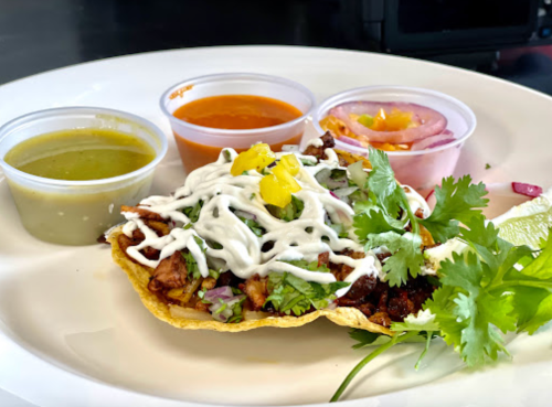 A plate with a taco topped with meat, lettuce, and sauce, accompanied by three small containers of salsa and onions.