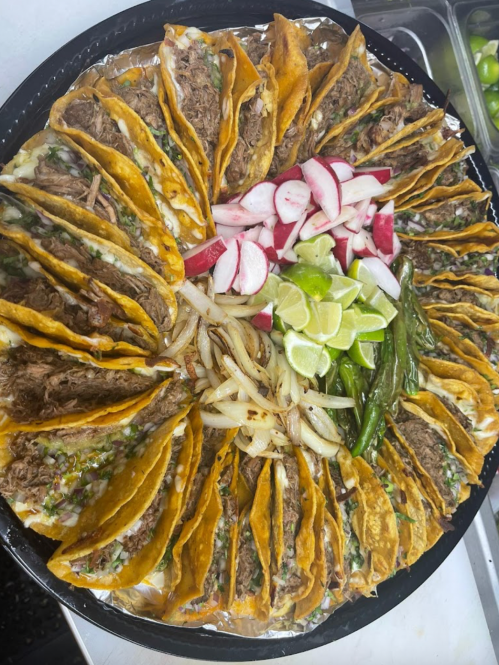 A large platter of tacos filled with beef, garnished with radishes, lime, onions, and green peppers.