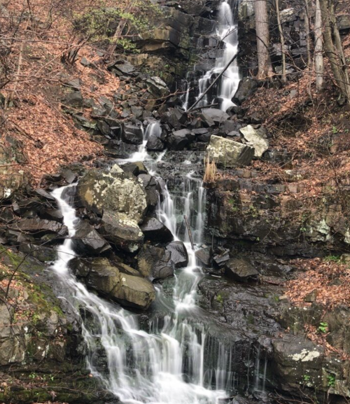 A serene waterfall cascading over rocky terrain, surrounded by autumn leaves and trees.