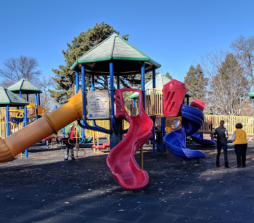 Colorful playground with slides and climbing structures, set against a clear blue sky and trees in the background.