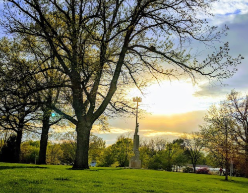 A serene park scene with trees and a monument, illuminated by a sunset in the background.