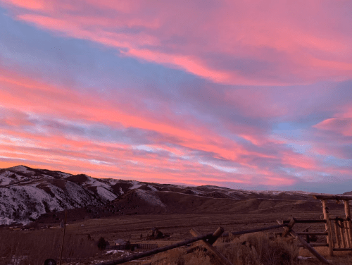 A vibrant sunset paints the sky in pink and purple hues over snow-capped mountains and a serene valley.