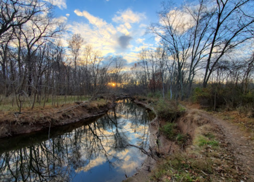 A serene river reflects the sky at sunset, surrounded by bare trees and a peaceful landscape.