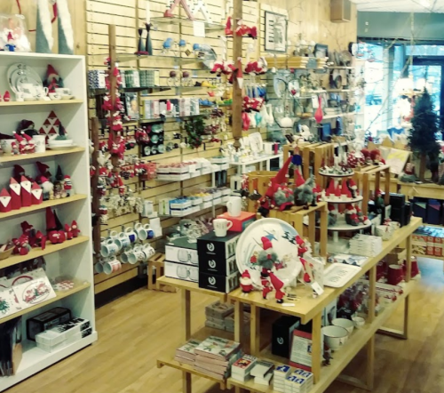 A cozy shop filled with festive decorations, holiday-themed items, and various gifts displayed on wooden shelves.