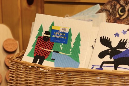 A basket of colorful Swedish dishcloths featuring playful designs of a man, a dog, and trees.