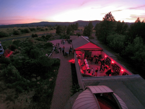 Aerial view of a building with red lighting, surrounded by people and nature at sunset.