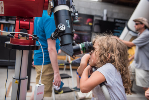 A child looks through a telescope while adults observe nearby at an outdoor astronomy event.