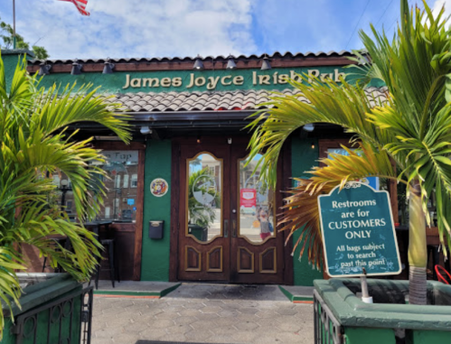 Entrance of James Joyce Irish Pub, surrounded by palm trees, with a sign indicating restrooms for customers only.
