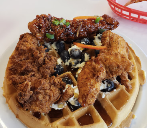 A plate of waffles topped with fried chicken, blueberries, and drizzled with syrup.