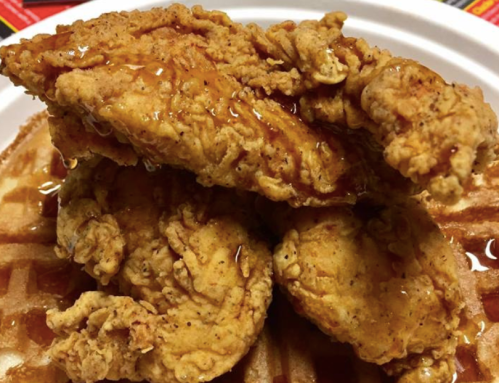 Three crispy fried chicken tenders drizzled with syrup, served on a waffle.