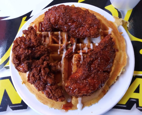 A plate of crispy fried chicken on a golden waffle, drizzled with syrup.