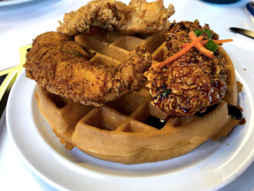 A plate featuring a golden waffle topped with two pieces of fried chicken, one spicy and one glazed, garnished with carrots.