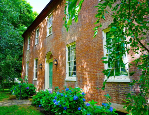 A charming brick house surrounded by greenery and blooming hydrangeas on a sunny day.