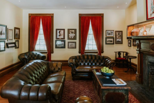 A cozy room with leather sofas, red curtains, framed photos on the walls, and a wooden coffee table with green apples.