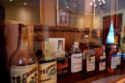 A display of vintage liquor bottles on a wooden shelf, showcasing various labels and designs.