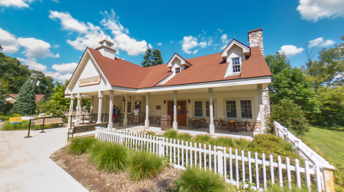 A charming building with a red roof and stone accents, surrounded by greenery and a white picket fence.