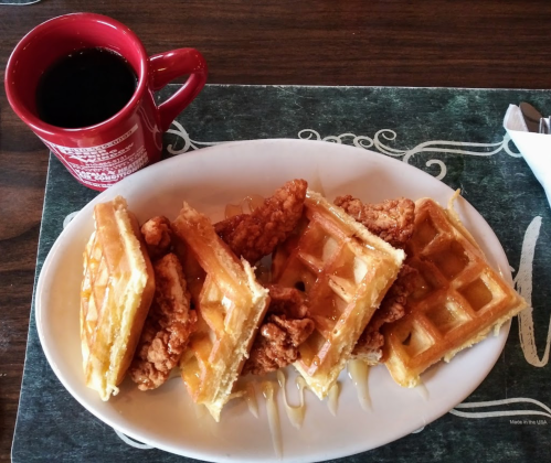 A plate of waffles topped with fried chicken and drizzled with syrup, alongside a red coffee mug.