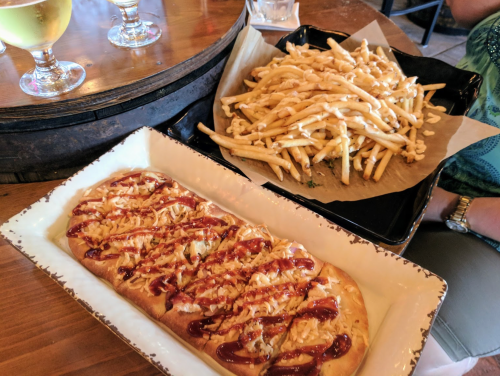 A flatbread topped with sauce next to a large serving of fries drizzled with cheese sauce on a wooden table.