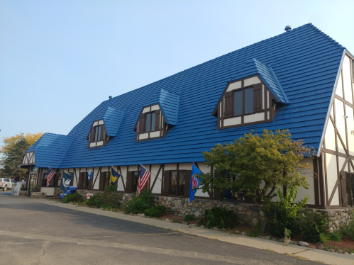 A large building with a blue roof and white walls, featuring multiple windows and flags, set against a clear sky.