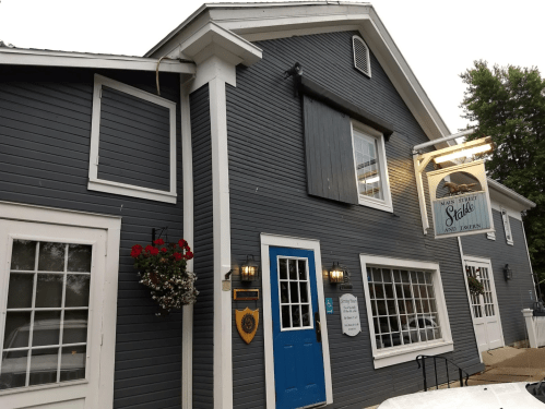 A gray building with a blue door, flower boxes, and a sign reading "Main Street Stables and Tavern."