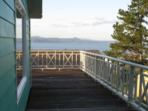 View from a wooden deck overlooking a calm lake and distant mountains under a clear sky.