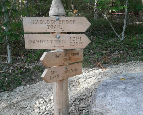 Wooden trail sign with arrows pointing to Hadlock Brook Trail and Sargent Mountain, showing distances in miles and kilometers.