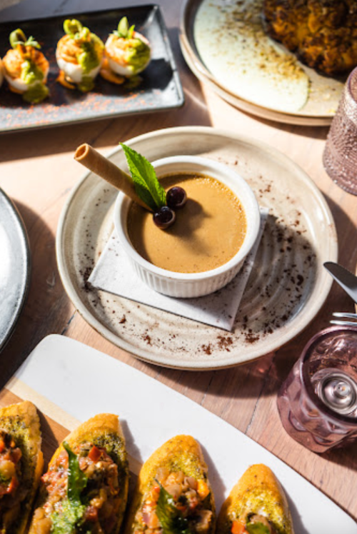 A plate of dessert with a creamy sauce, garnished with mint and berries, alongside various appetizers on a table.