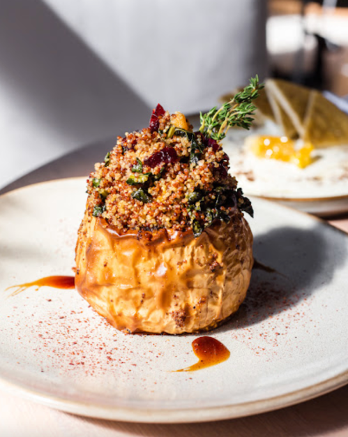 A plated dish featuring a stuffed baked apple topped with herbs and a sprinkle of spices, served on a light-colored plate.