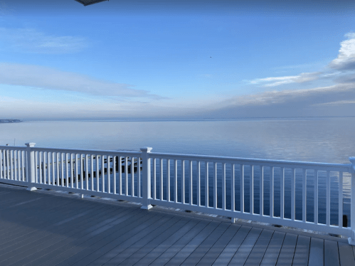 A serene view of calm water and a clear sky from a deck with a white railing.