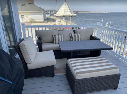 Cozy outdoor seating area with a sectional sofa, coffee table, and striped ottoman overlooking a waterfront view.