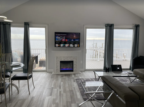 Cozy living space with a view of the water, featuring a TV, fireplace, dining area, and large windows.