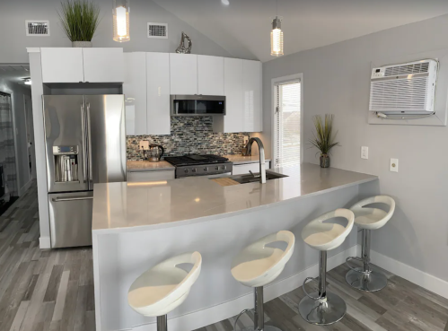 Modern kitchen with stainless steel appliances, a large island, and four white bar stools. Bright and airy design.