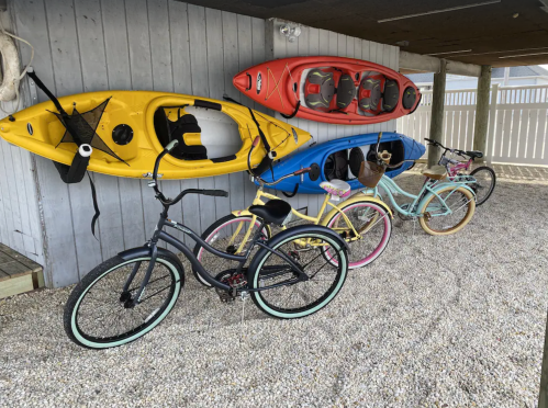 A row of colorful bicycles and kayaks hanging on a wall, set against a gravel surface.