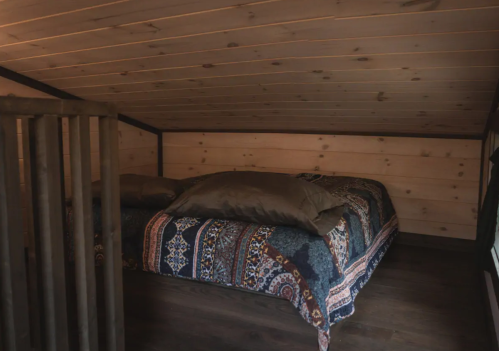 Cozy loft bedroom with a wooden ceiling, featuring a bed with decorative pillows and a patterned blanket.
