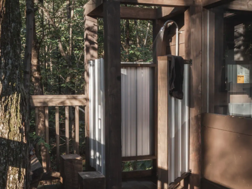 Outdoor shower area made of wood and metal, surrounded by trees in a natural setting.