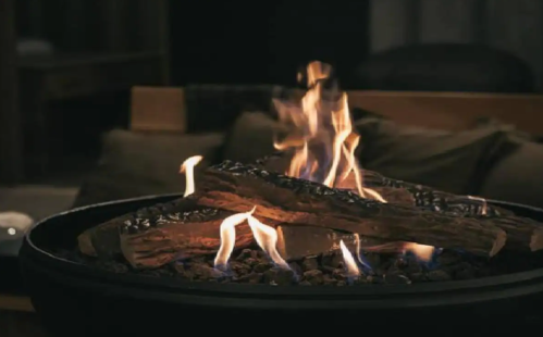 A cozy fire burns in a modern fireplace, with logs and glowing flames creating a warm atmosphere.