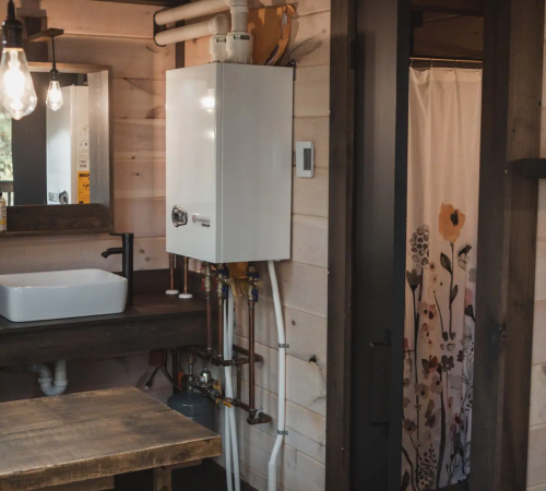A cozy bathroom with a white water heater, sink, and a floral shower curtain in a wooden interior.
