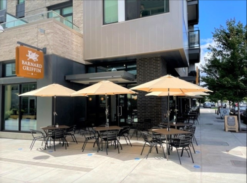 Outdoor dining area with tables and umbrellas at Barnard Griffin, featuring modern architecture and a clear blue sky.