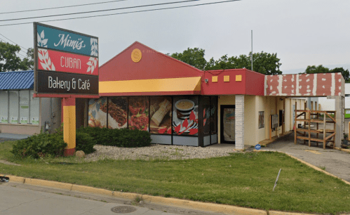 A colorful building with a sign reading "Mimi's Cuban Bakery & Café," featuring outdoor seating and a landscaped area.