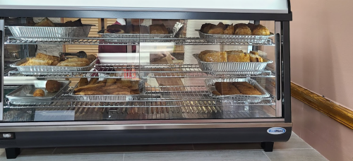 A display case filled with various baked goods in aluminum trays, showcasing pastries and bread.