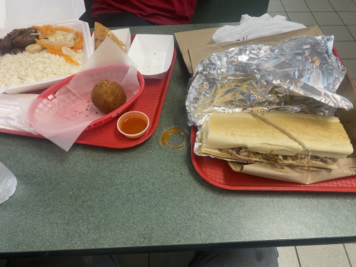 Two red trays with food: one has rice, meat, vegetables, and a falafel; the other has a sandwich wrapped in foil.