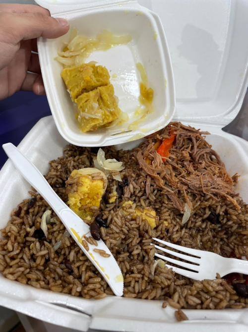A takeout container with rice, shredded meat, and a hand holding a small container of yellow food.