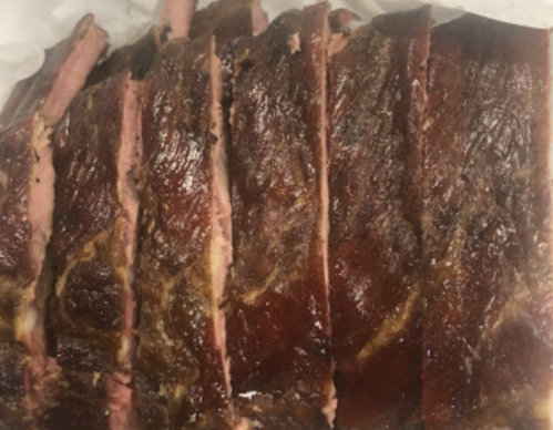 Sliced smoked meat with a dark, caramelized crust, arranged neatly on a white surface.