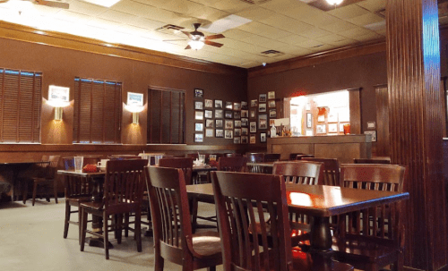 Cozy restaurant interior with wooden tables, chairs, and framed photos on the walls, creating a warm atmosphere.