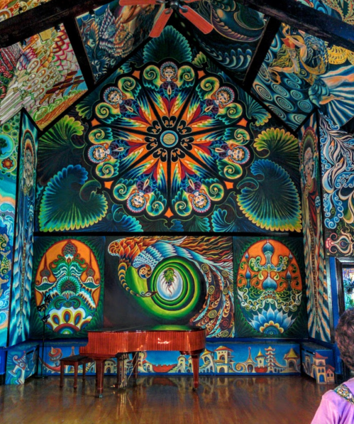 Vibrant, colorful mural covering the walls of a room with a wooden piano in the foreground.