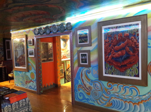 Colorful interior featuring vibrant murals and framed artwork on the walls, with a bright orange doorway in the background.