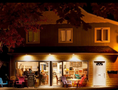 A cozy shop at night, illuminated with warm lights, featuring colorful chairs outside and a welcoming atmosphere.