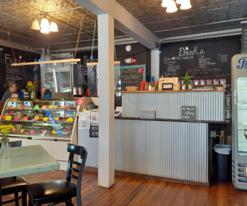 A cozy café interior with a counter, display case of pastries, chalkboard menus, and seating.