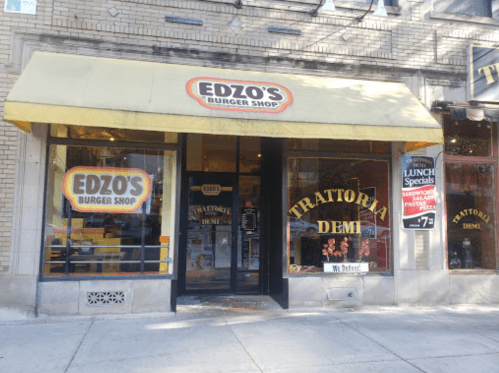 Exterior of Edzo's Burger Shop with a yellow awning and large windows displaying the restaurant's name and menu specials.