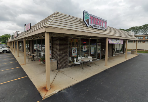 Exterior view of Tizzy's Treats & Eats, a casual eatery with outdoor seating and a sign on a cloudy day.